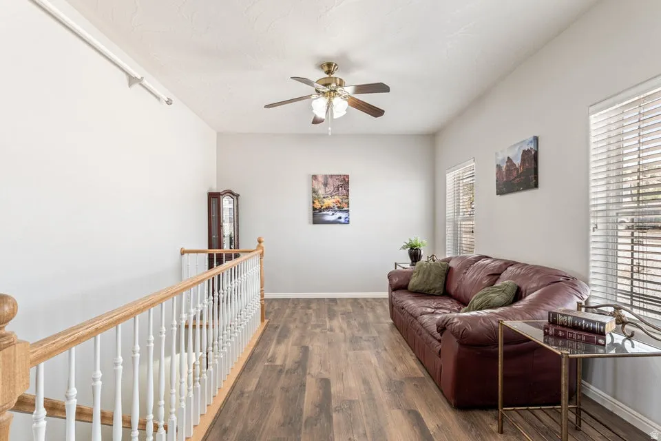 Spacious loft area featuring wood-finish flooring, a ceiling fan with integrated lighting, and multiple windows with blinds