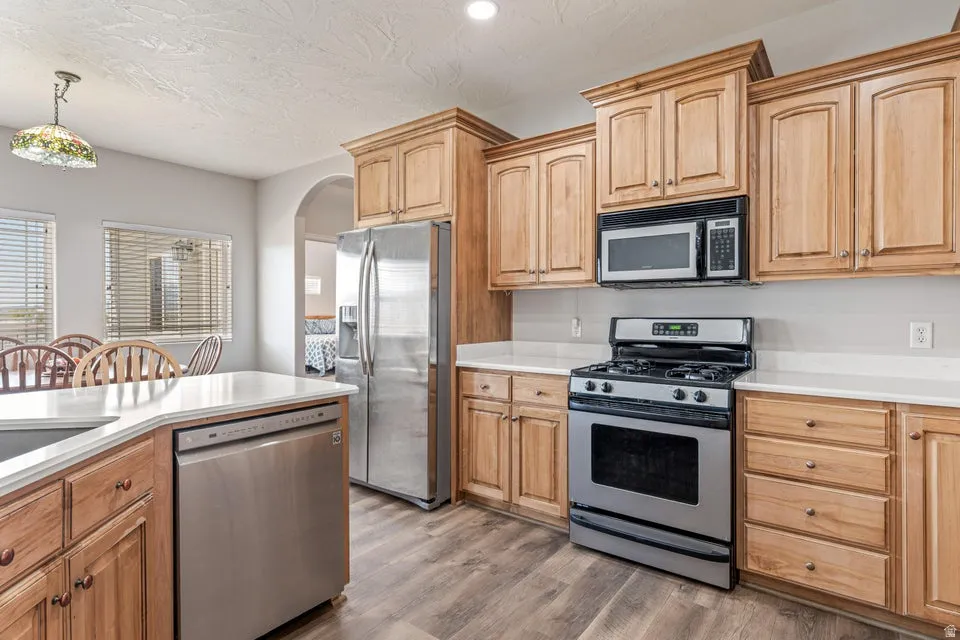 Kitchen featuring wood cabinetry, stainless steel appliances, light-toned countertops, and wood-finish flooring