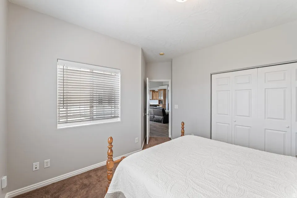 Bedroom featuring light gray walls, brown carpet flooring, a white window with horizontal blinds, and a built-in closet with white bifold doors