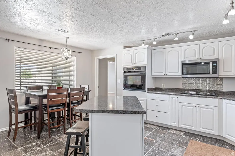 Kitchen featuring white cabinetry, dark stone countertops, stainless steel microwave, and built-in oven