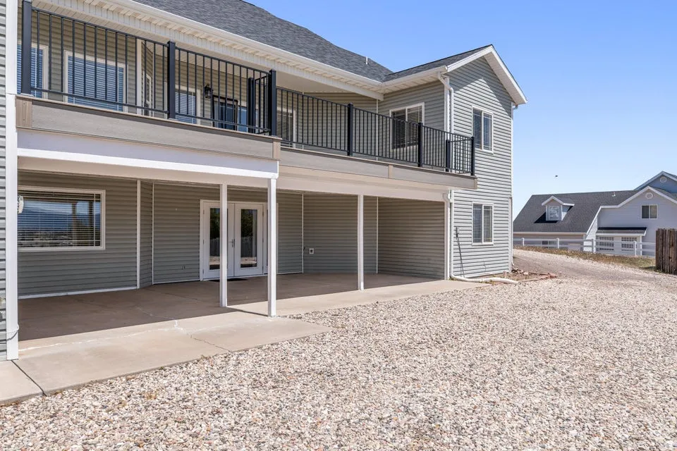 Exterior featuring light gray siding, a second-story balcony with dark railings, and a covered concrete patio