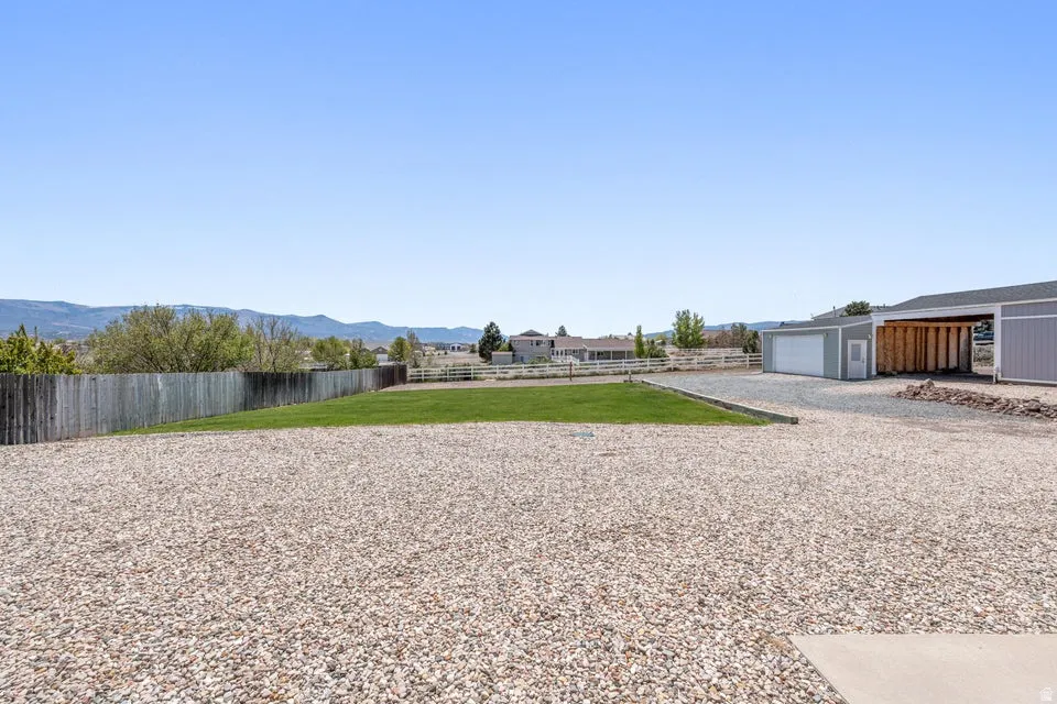 Expansive gravel yard with a dedicated grassy area, a detached garage, and a covered carport structure