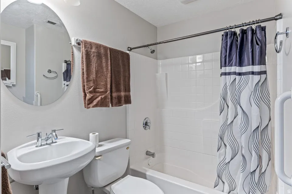 Bathroom featuring a pedestal sink with chrome fixtures, a circular wall mirror, and a full-size bathtub with a shower and white subway tile surround