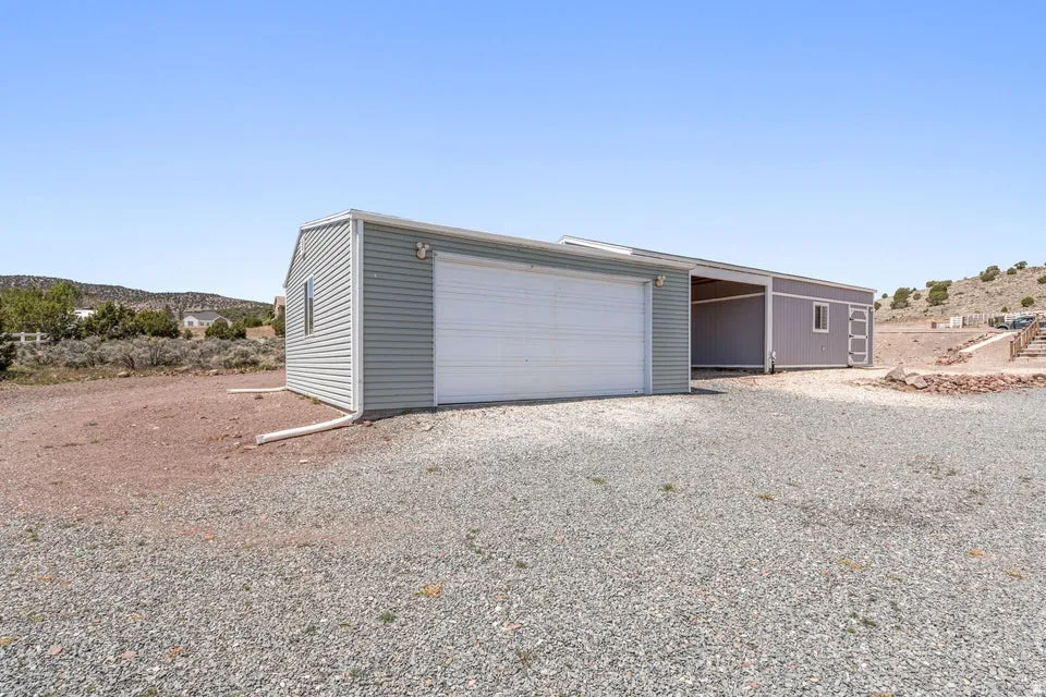 Detached utility building featuring corrugated metal siding, a single garage door, and an open covered area
