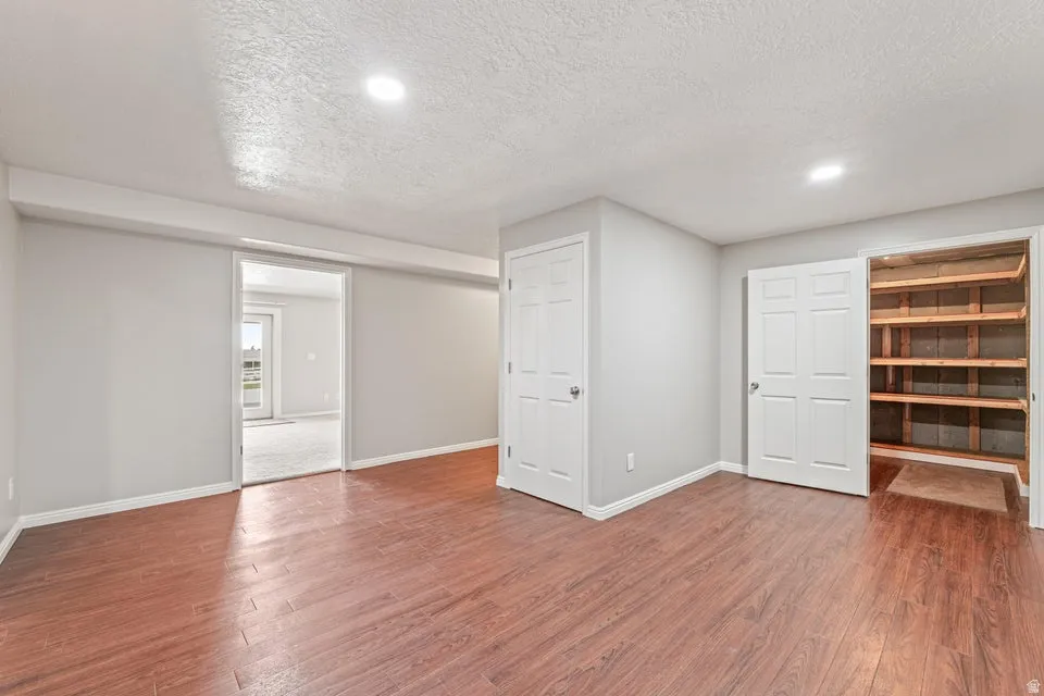 Spacious room featuring wood-finish flooring, light grey walls, recessed lighting, and a large built-in storage closet with wood shelving