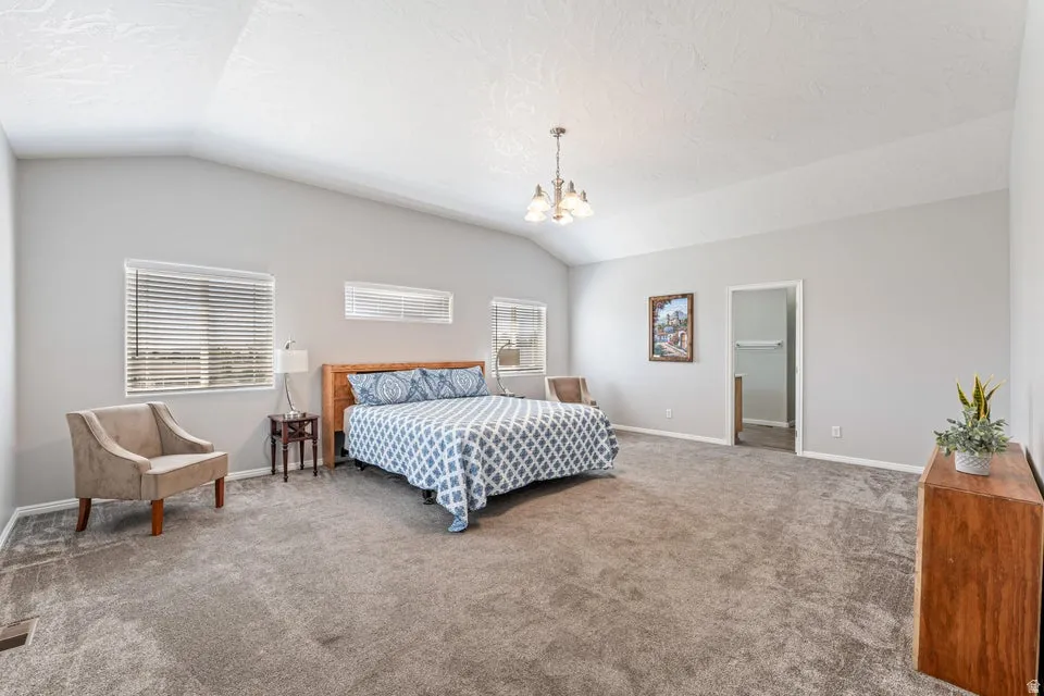 Spacious room featuring vaulted ceilings, neutral-toned carpeting, multiple windows for natural light, and a built-in chandelier