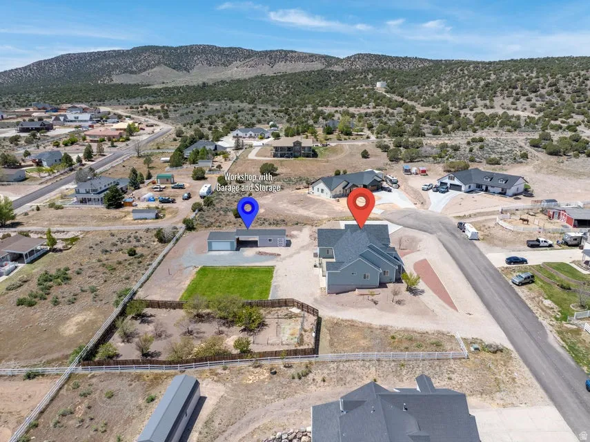 Spacious property featuring a light gray residence with a dark gray roof, a separate workshop structure with a garage door, a manicured lawn area, and a fenced perimeter