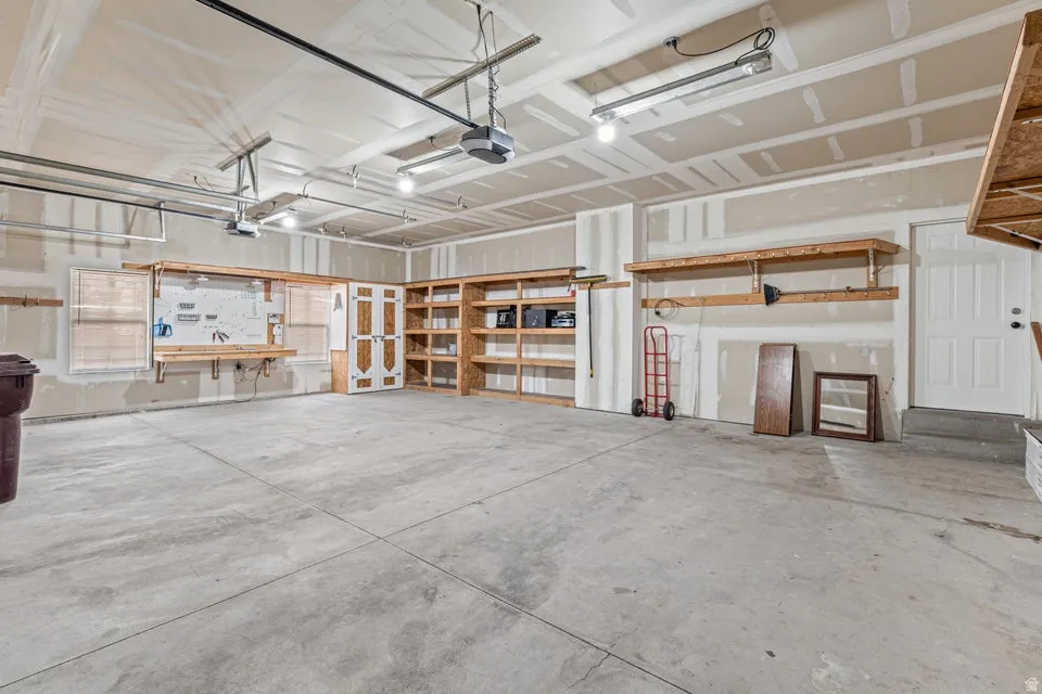 Spacious garage featuring a concrete floor, built-in shelving, a dedicated workbench area, overhead lighting, and two garage door openers