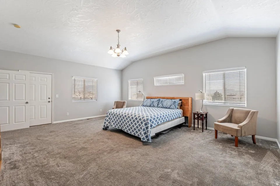 Spacious room featuring vaulted ceilings, a chandelier, multiple windows with blinds, a two-panel door, and neutral-toned wall paint