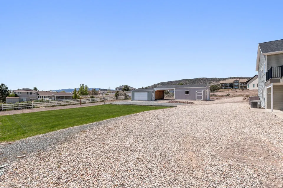 Expansive gravel area and a manicured lawn, featuring a detached garage with an attached carport