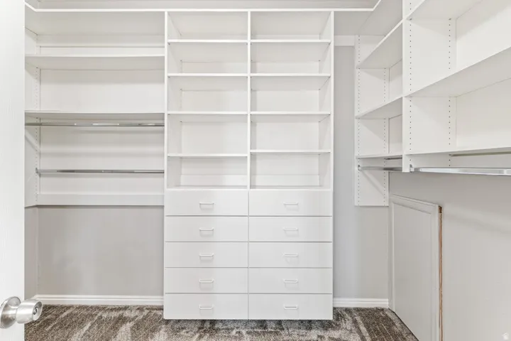Custom walk-in closet featuring white built-in shelving, multiple hanging rods, and integrated drawer storage