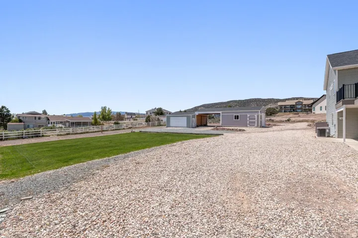 Expansive gravel area and a manicured lawn, featuring a detached garage with an attached carport