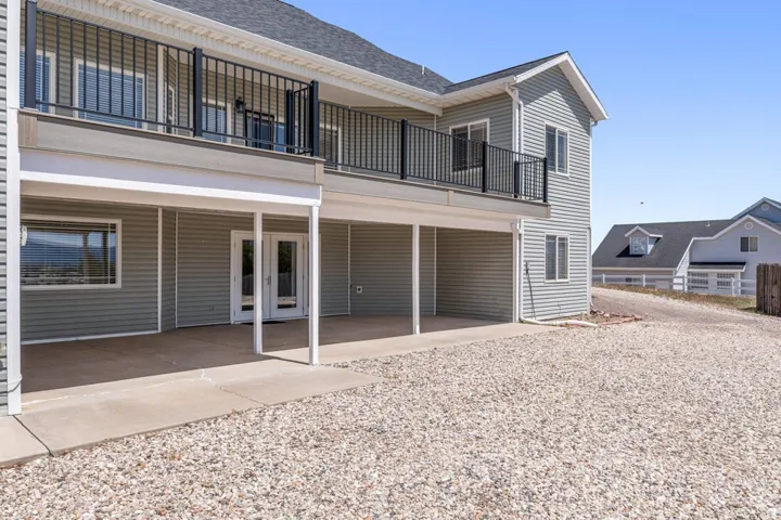 Exterior featuring light gray siding, a second-story balcony with dark railings, and a covered concrete patio