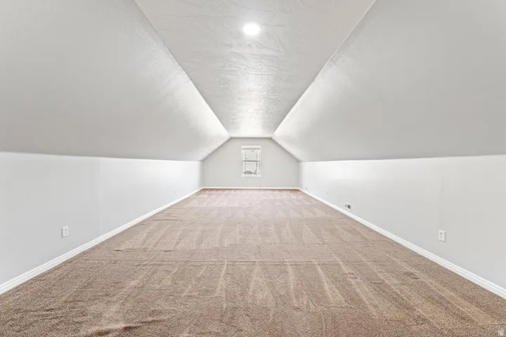 Expansive carpeted room featuring a vaulted ceiling with recessed lighting, white baseboards, and a rear window