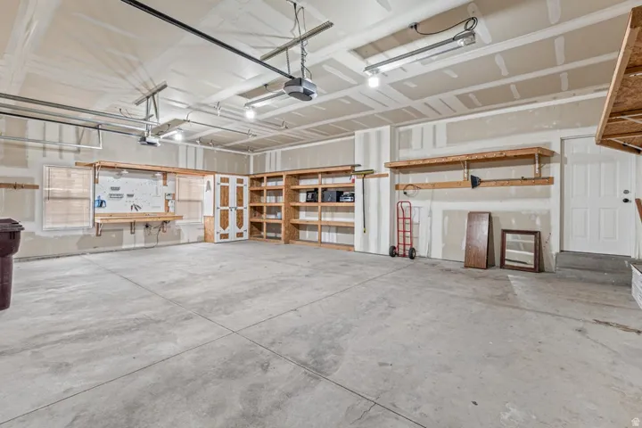 Spacious garage featuring a concrete floor, built-in shelving, a dedicated workbench area, overhead lighting, and two garage door openers