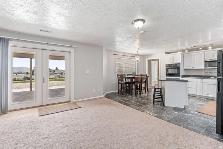 Open-concept living space featuring a carpeted area, French doors leading to an exterior patio, and a dining area with a chandelier