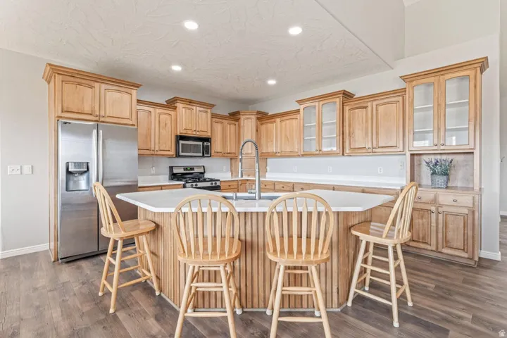 Kitchen featuring wood-finish cabinetry, stainless steel appliances, a center island with countertop seating, white countertops, and wood-finish flooring