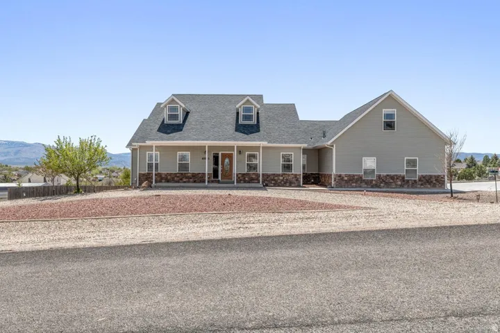 Two-story residence featuring light gray siding with a stone-clad foundation, a covered front porch, and a dark shingle roof with two dormer windows