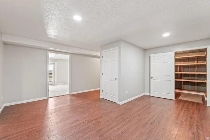 Spacious room featuring wood-finish flooring, light grey walls, recessed lighting, and a large built-in storage closet with wood shelving