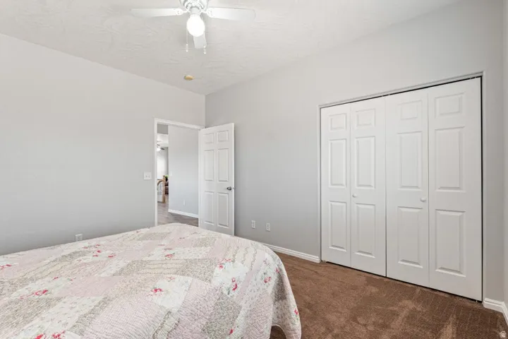 Neutral-toned room featuring a white ceiling fan with light fixture, light gray painted walls, and brown carpet flooring