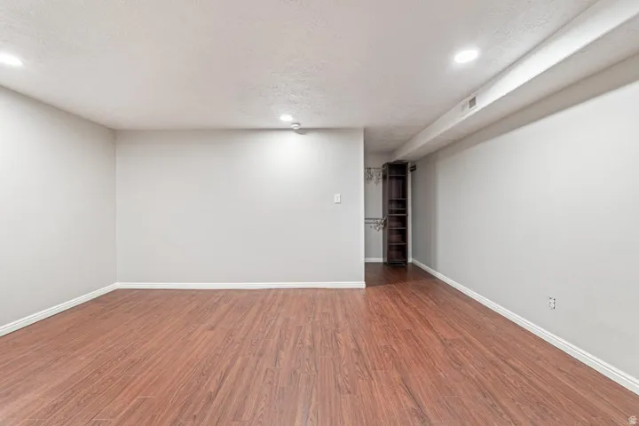 Spacious room featuring wood-finish flooring, recessed ceiling lighting, light gray wall paint, white baseboards, and built-in shelving