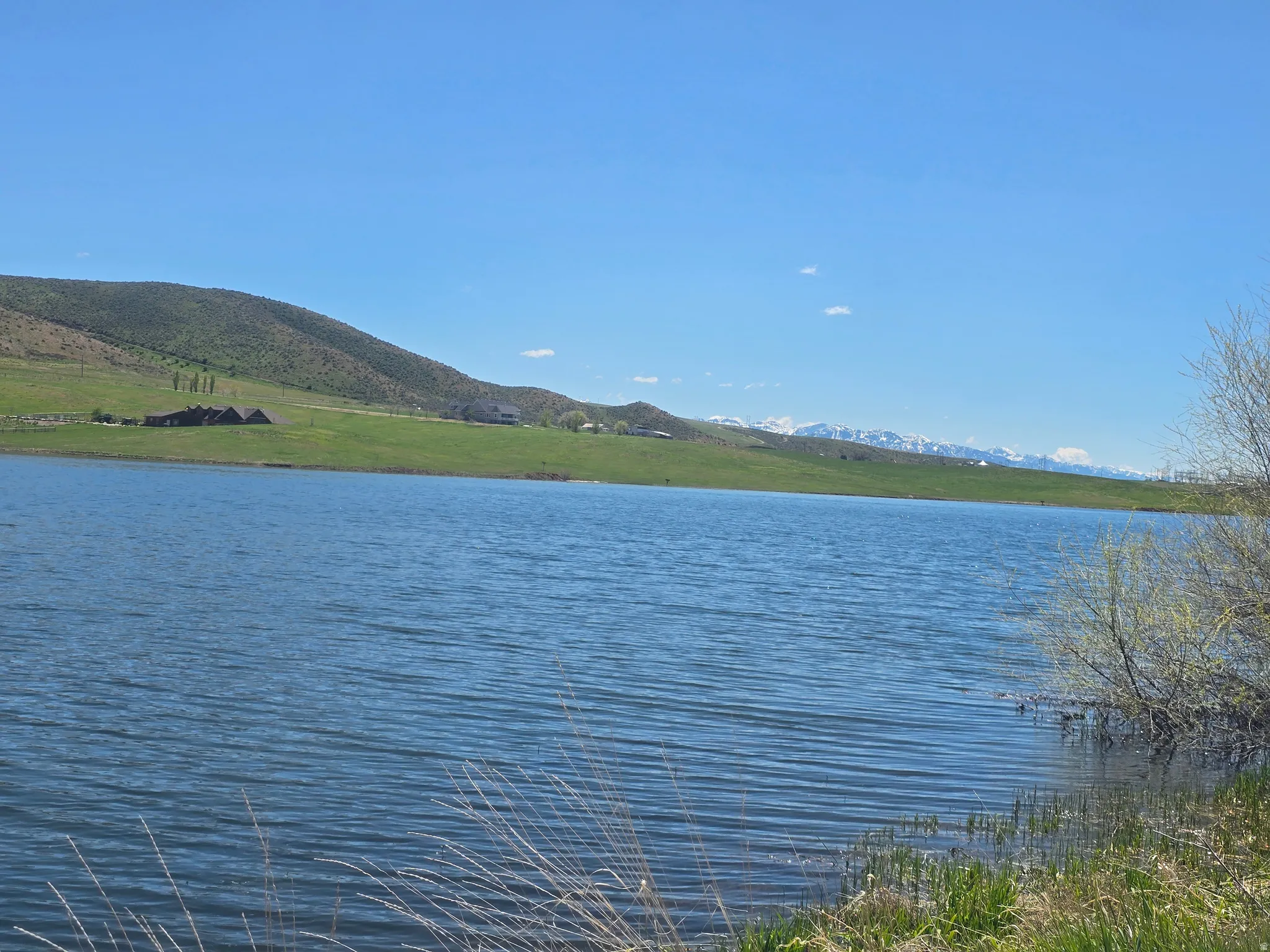 Expansive water frontage with a verdant hillside backdrop, distant mountain peaks, and clear sky