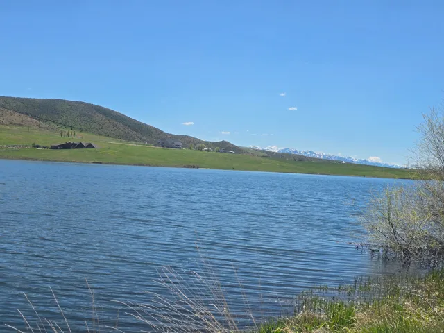 Expansive water frontage with a verdant hillside backdrop, distant mountain peaks, and clear sky