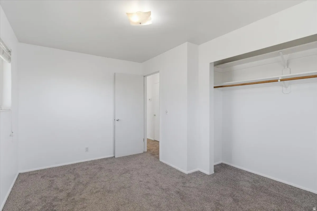 Carpeted room featuring a ceiling-mounted light fixture, white walls, and a window with blinds
