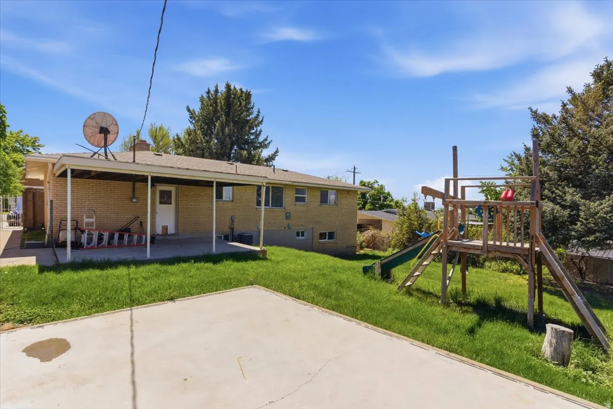 Expansive backyard featuring a covered patio, a large concrete pad, established grassy areas, and mature trees