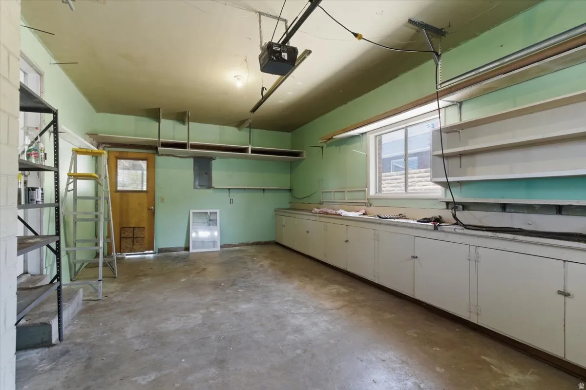 Spacious garage featuring a concrete floor, built-in lower cabinetry, a window offering natural light, an overhead garage door opener, and wall-mounted shelving