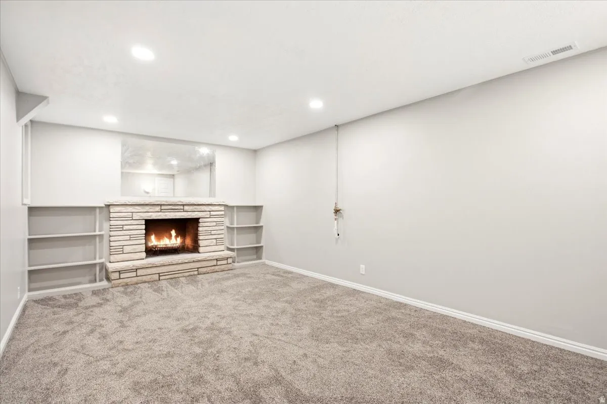 Stone-clad fireplace with a hearth and built-in shelving, complemented by recessed lighting and wall-to-wall carpeting