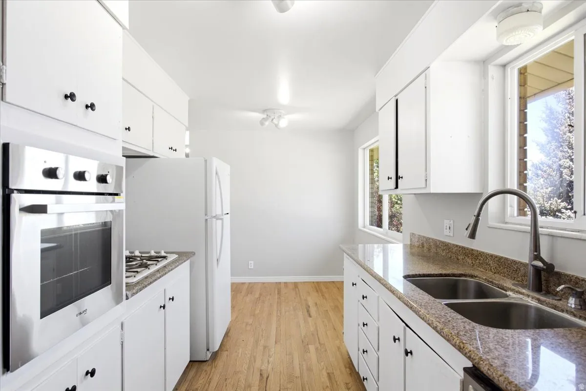 Kitchen featuring dual basin stainless steel sink, wall-mounted oven, gas cooktop, white cabinetry with black hardware, and wood-finish flooring