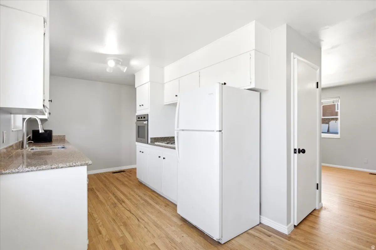 Kitchen featuring white cabinetry, light countertops, wood-finish flooring, built-in oven, and a white refrigerator