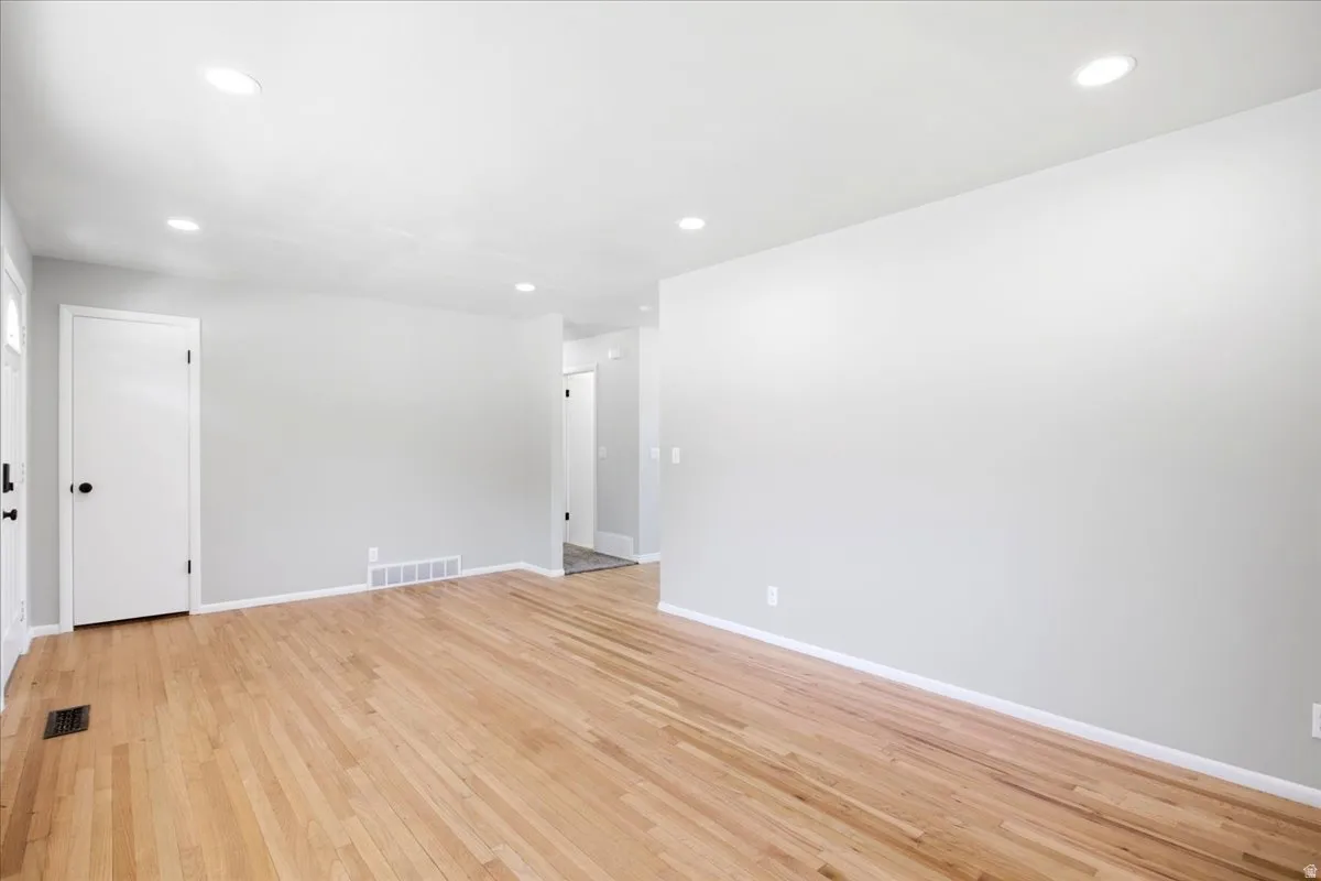 Spacious room featuring wood-finish flooring, light grey painted walls, white trim, recessed lighting, and a white interior door with black hardware
