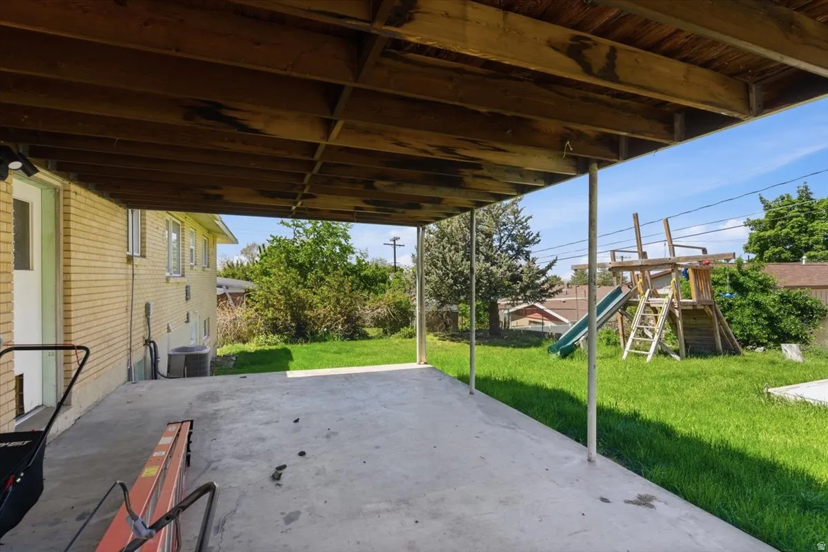 Covered concrete patio with overhead wood beam structure, leading to a grass lawn
