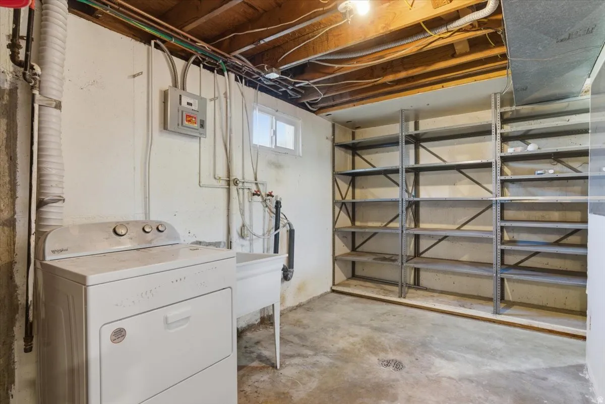 Basement utility area featuring exposed wood beam ceiling, concrete flooring, a utility sink, and built-in metal shelving