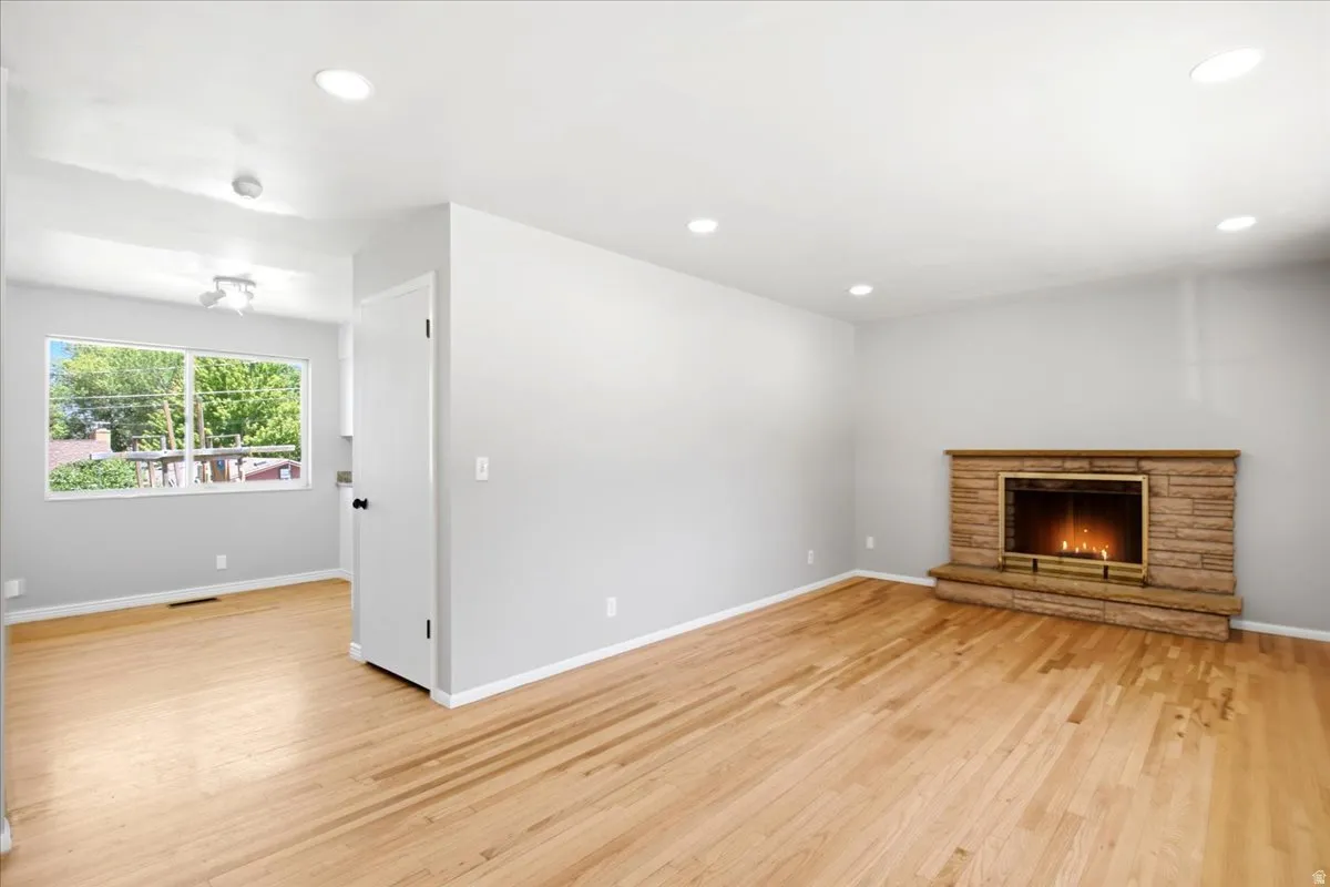 Spacious living area featuring wood-finish flooring, a stone-clad fireplace with a brass firebox, and recessed lighting