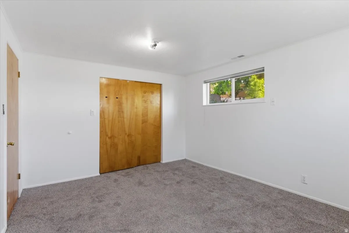 Room featuring gray carpet flooring, white painted walls, a horizontal window, and wood-finish bi-fold closet doors