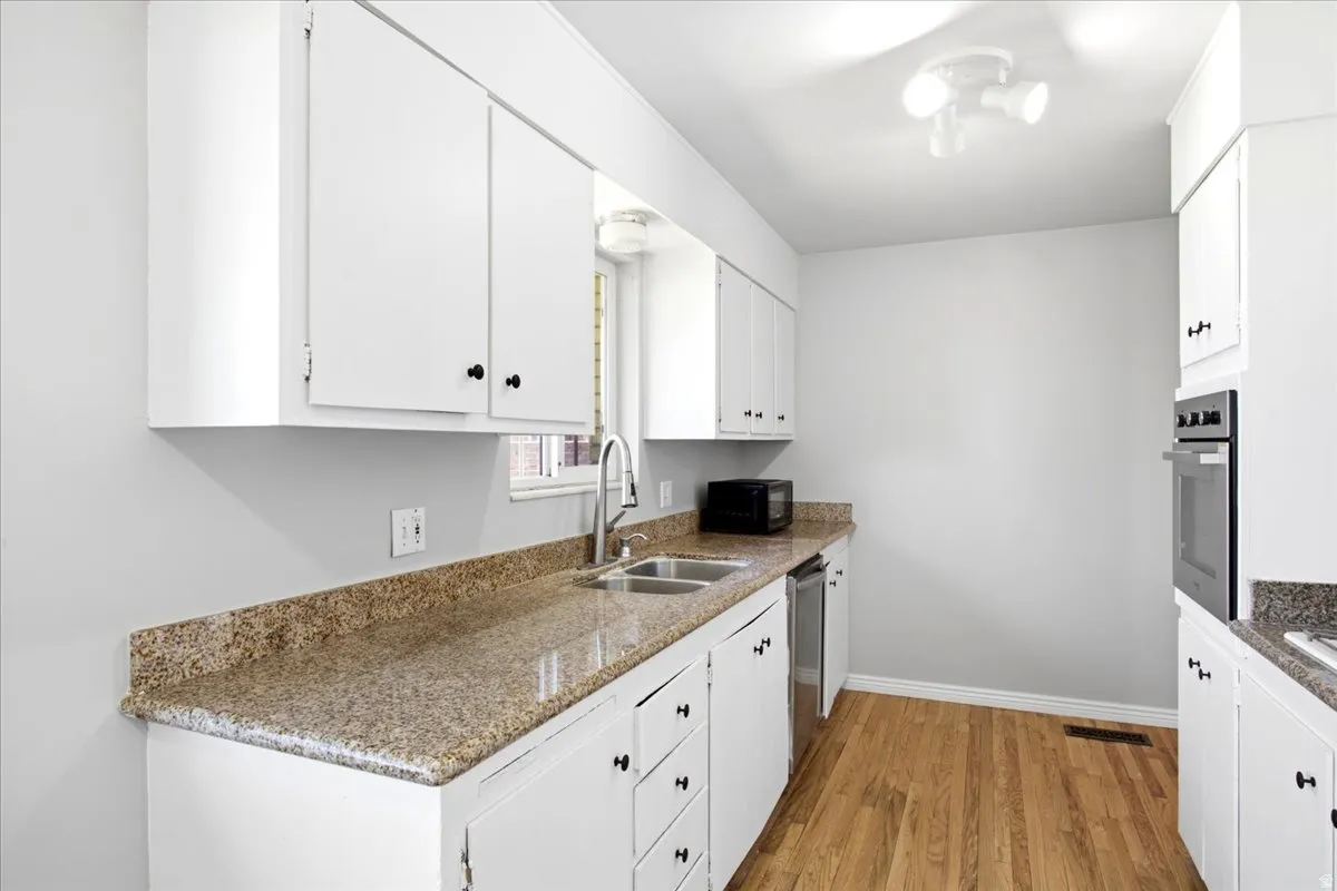 Kitchen featuring white cabinetry, granite-finish countertops, a double basin sink with a high-arc faucet, wood-finish flooring, and a built-in oven