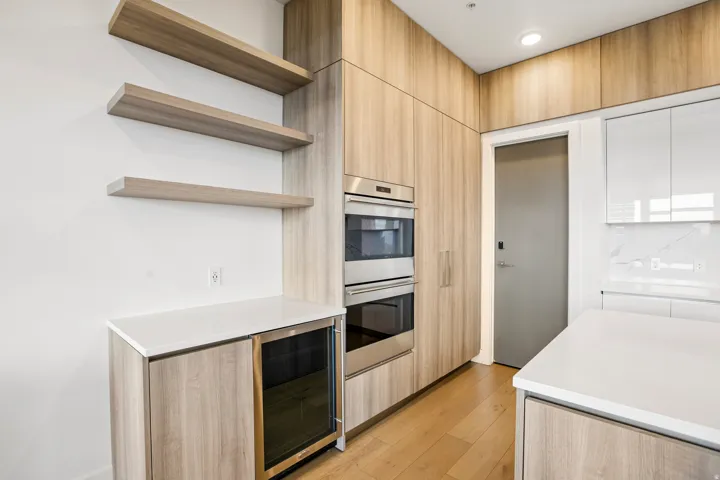Modern kitchen featuring wood-finish cabinetry, integrated stainless steel double ovens, and a beverage cooler