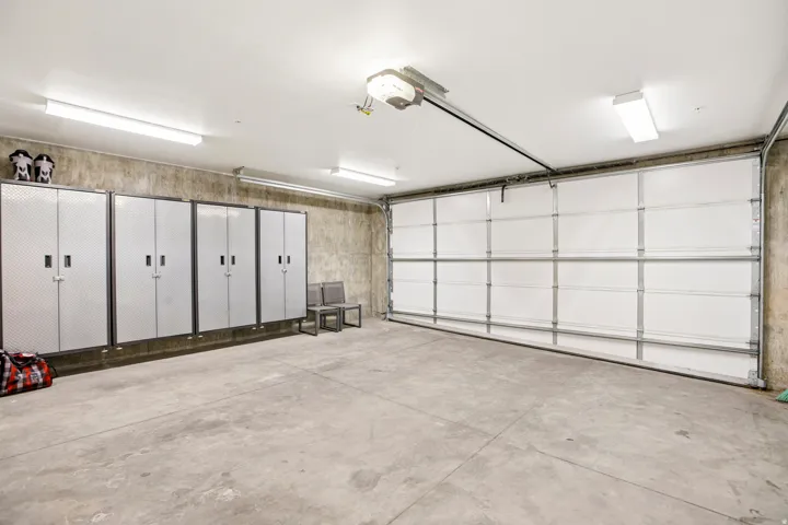 Spacious garage featuring a concrete floor, overhead lighting, an automatic garage door, and built-in storage cabinets