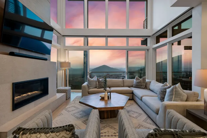 Living area featuring a floor-to-ceiling window wall, a linear fireplace with a textured surround, light-tone wood-finish flooring, and a mountain backdrop