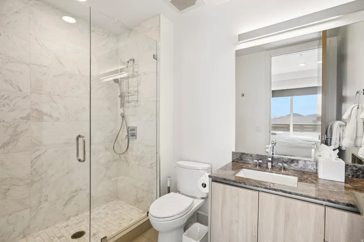 Contemporary bathroom featuring a glass-enclosed shower with large format wall tiles and a mosaic tile floor, an integrated vanity with wood-finish cabinetry, a stone countertop, and a rectangular undermount sink with a wall-mounted mirror