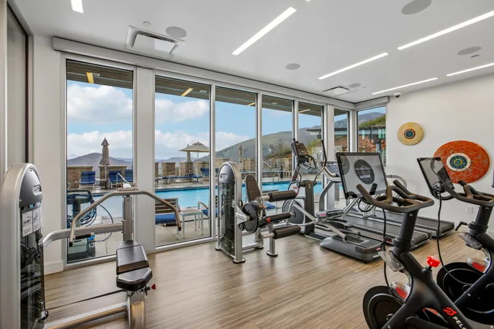 Fitness center with wood-finish flooring, ample natural light from floor-to-ceiling windows, and recessed ceiling lighting