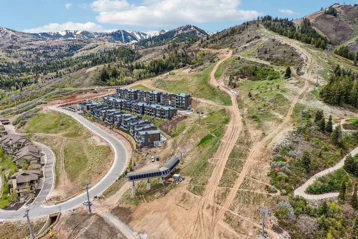 Contemporary multi-story residences featuring dark facades and flat roofs, situated on a sloped terrain with paved roads