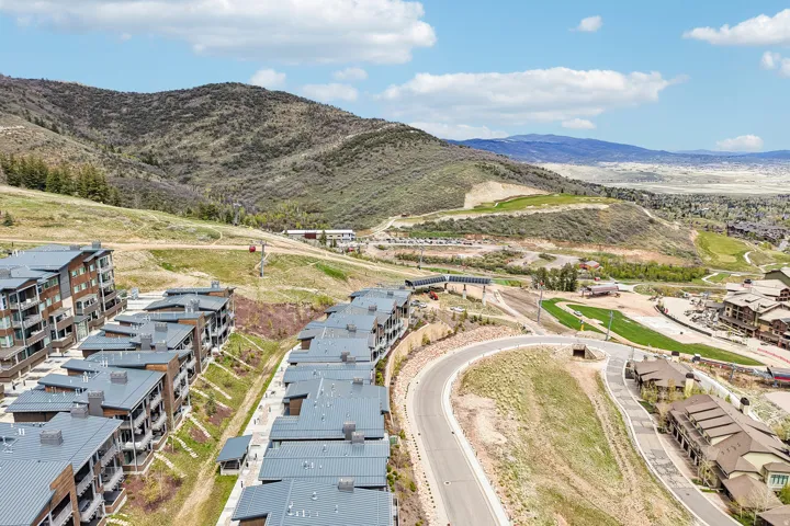 Modern multi-story buildings featuring balconies and dark grey roofs set against a mountainous backdrop