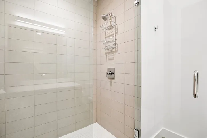 Shower enclosure featuring a frameless glass door, light-toned horizontal tile, a built-in shower bench, and a tiled shower pan