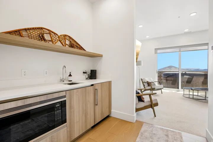 Contemporary wet bar with light wood-finish cabinetry, built-in microwave, white countertop, and stainless steel sink