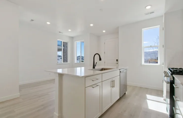 Open-concept kitchen featuring a central island with a sink and white cabinetry, stainless steel dishwasher, a gas range, recessed lighting, and light wood-finish flooring