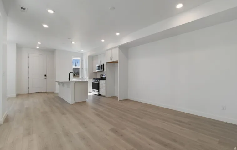 Open-concept living space featuring wood-finish flooring, recessed lighting, and a white kitchen island with a black faucet